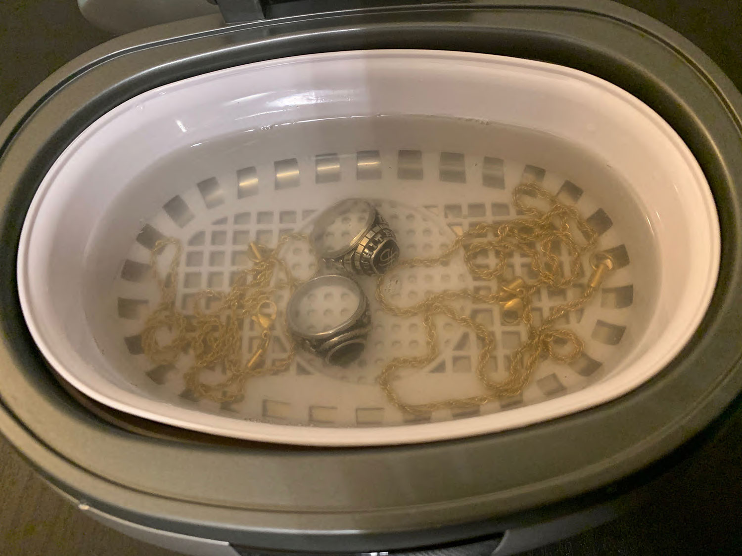 Magnasonic Ultrasonic Jewelry Cleaner product image showing jewelry in tank after a cycle. The water is murky from all the dirt and residue removed.